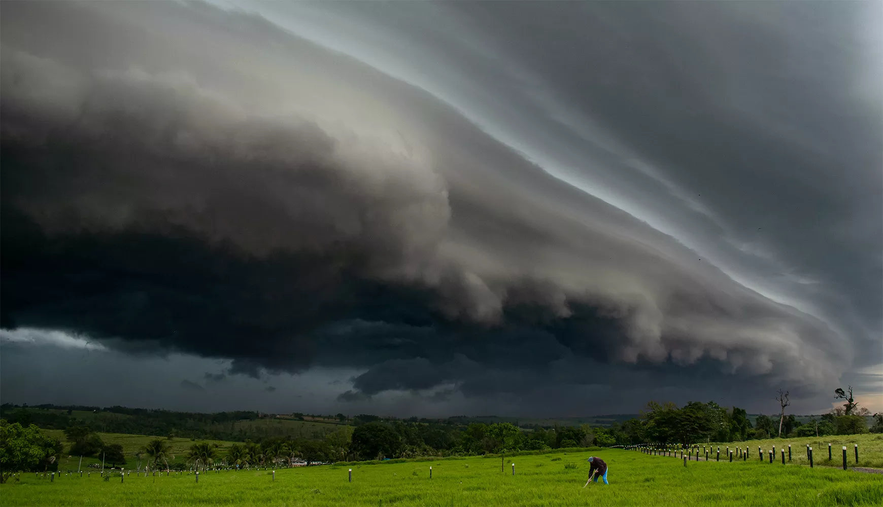 a dark storm approaches on the horizon behind a man digging a hole in a field